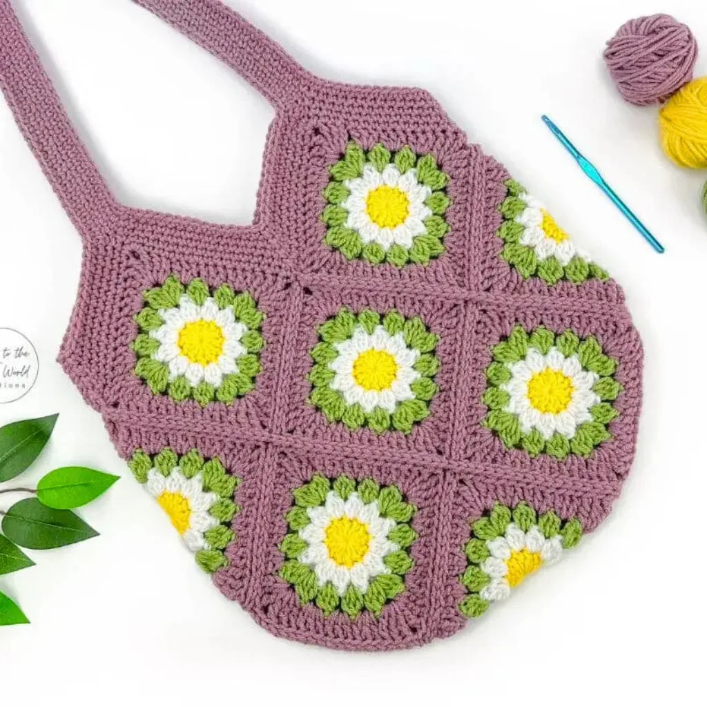 A crochet shoulder bag featuring a daisy granny square, with a crochet hook and a ball of yarn beside it.