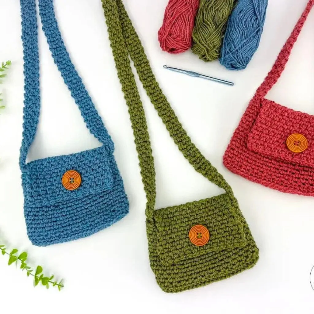 Three small crochet crossbody bags with large wooden button closures, made using the moss stitch.