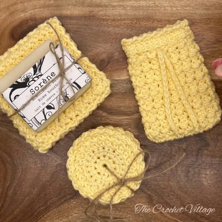 A crochet spa set featuring textured washcloths, a soap bag, and face pads, displayed alongside a plant, soap, and a bathroom container. Perfect for a luxurious, handmade self-care experience.
