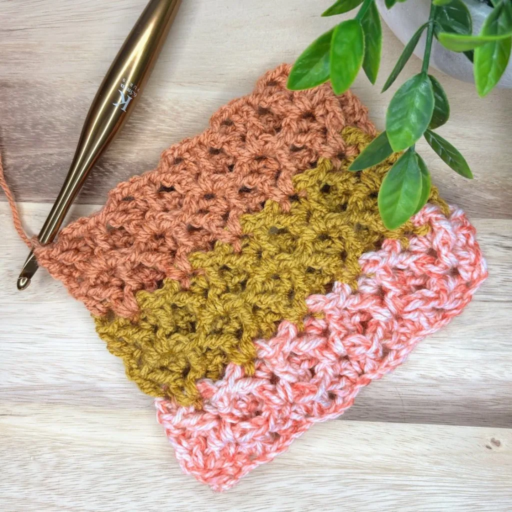 A close-up of a crochet piece with a textured stitch, accompanied by a crochet hook, resting on a wooden surface