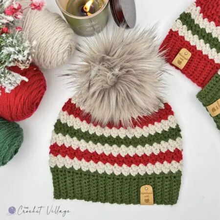 free crochet Christmas hat pattern - Winter Sled Beanie striped in red, green and cream with a ribbed brim and faux fur pom pom