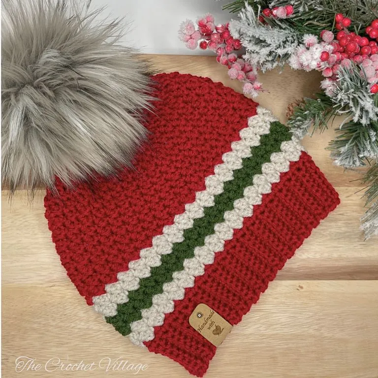 red crochet Christmas beanie with a single green and cream stripe band, ribbed brim and faux fur pom pom