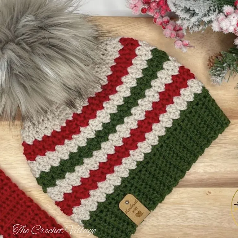 close up of the textured stitch on a striped crochet Christmas beanie in red, green and cream with a faux fur pom pom