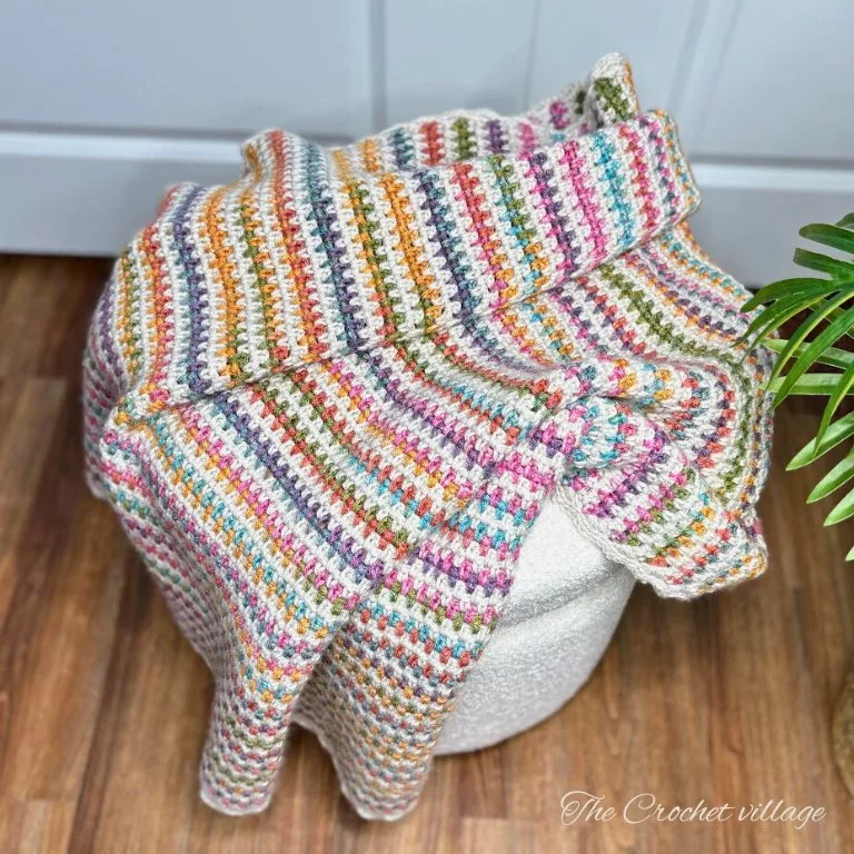 A colorful striped moss stitch crochet throw blanket folded neatly on a chair.