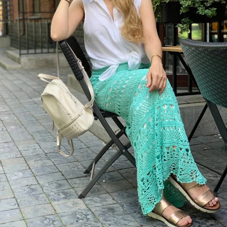 A woman sitting on a bench wearing a stunning crochet maxi skirt with elegant, flowy lace details that add femininity and charm to her outfit