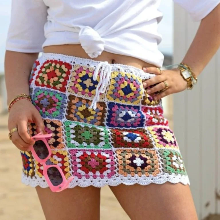 A woman holding sunglasses and wearing a cute, summery crochet granny square skirt, perfect for a fun, casual look.