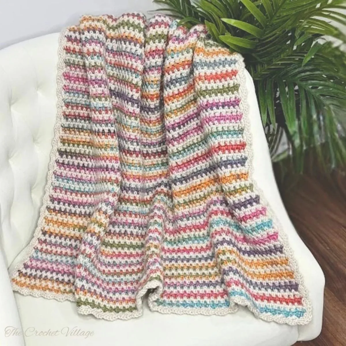 rochet moss stitch lap blanket draped over a white tufted chair with a scalloped cream border