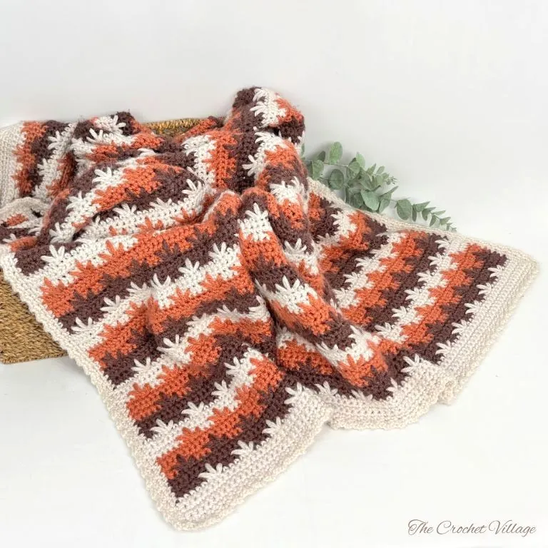 Cozy crochet afghan in warm fall colors, draped over a chair, featuring autumn leaves in rich shades of orange, brown, and beige