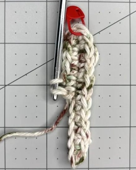 Close-up of a crochet piece in progress with a stitch marker attached and a crochet hook beside it.