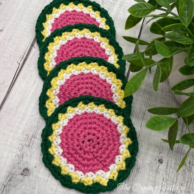 Four round crochet watermelon coasters in pink, green, yellow, and white.