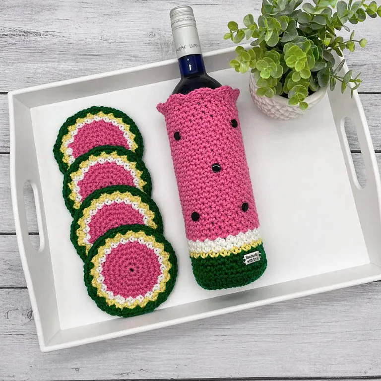 Crochet watermelon wine cozy with matching coasters displayed in a white tray on a rustic wooden surface- free melon wine cozy pattern