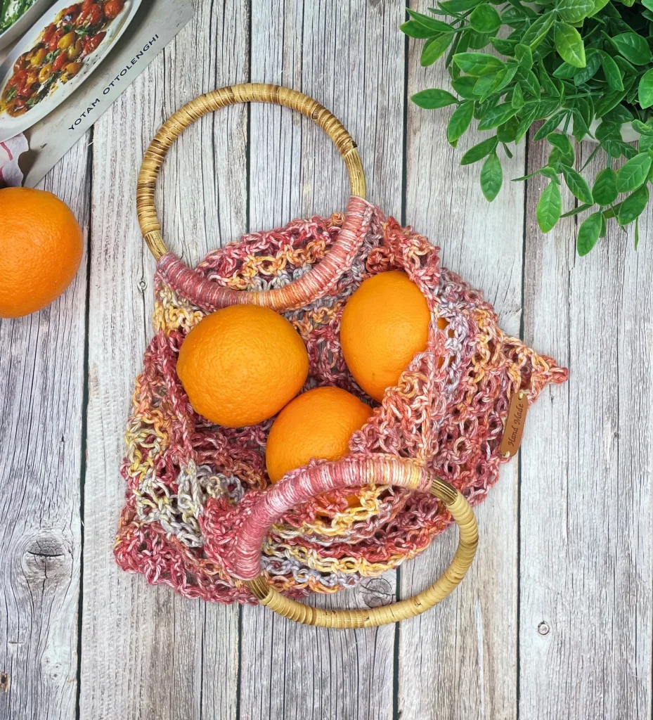 Crochet produce bag with Solomon’s Knot stitch and round wooden handles filled with oranges
