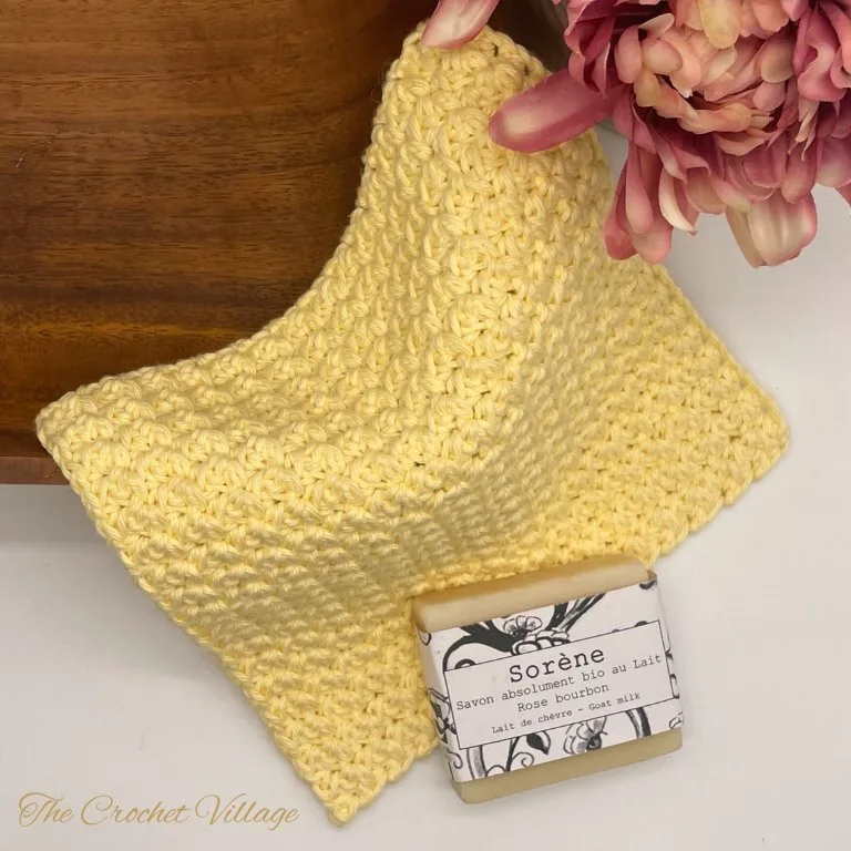 A textured, reusable crochet washcloth displayed with a bar of soap—an eco-friendly and handmade addition to any bath routine.