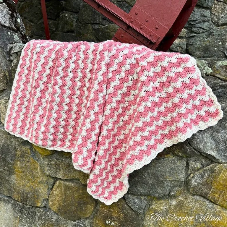 A gorgeous two-color baby blanket featuring a starburst stitch, draped over a wall