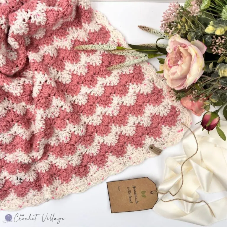 Close-up of the textured shell stitch pattern in a pink and cream crochet blanket