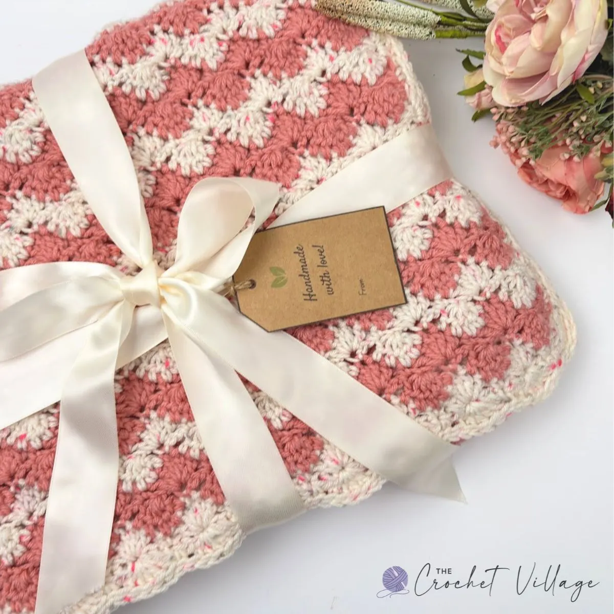 Magnolia free crochet blanket pattern in rose pink and cream, folded with a satin ribbon and handmade gift tag