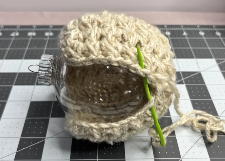 A plastic bauble inserted into a crochet piece being sewn closed to form a crochet ornament.