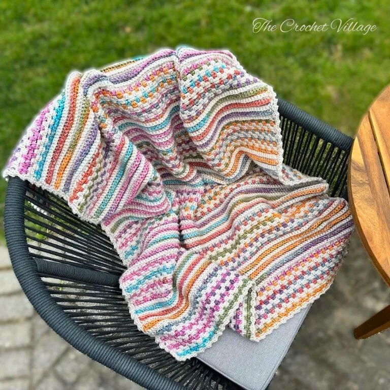 Crochet blanket with textured stitches and colorful stripes draped over a chair outdoors – reversible and easy crochet blanket pattern.
