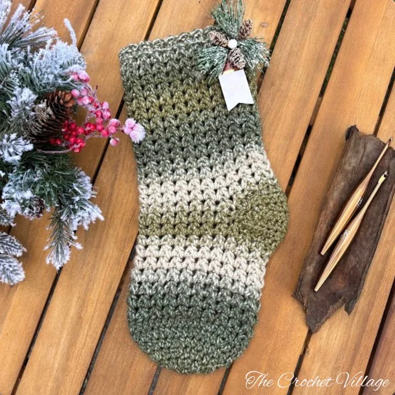 Oversized crochet Christmas stocking on a wooden surface, accompanied by a crochet hook and festive Christmas décor.