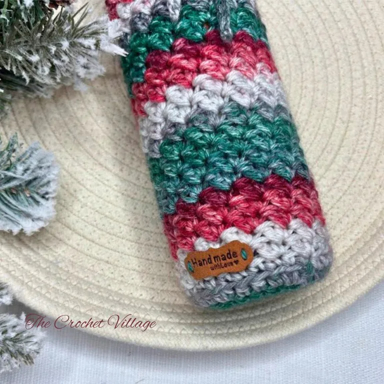 Close-up of a crochet wine bottle cover showcasing a beautifully textured stitch pattern, with festive holiday details in the background.