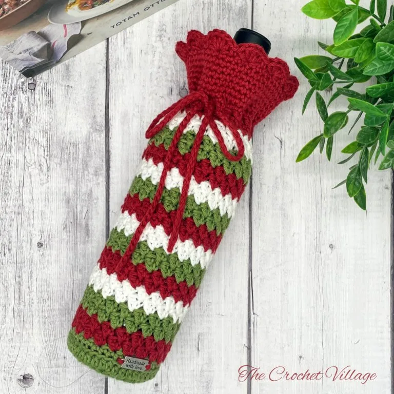 A crochet wine bottle cover showcasing a beautifully textured stitch pattern, with festive holiday details in the background.