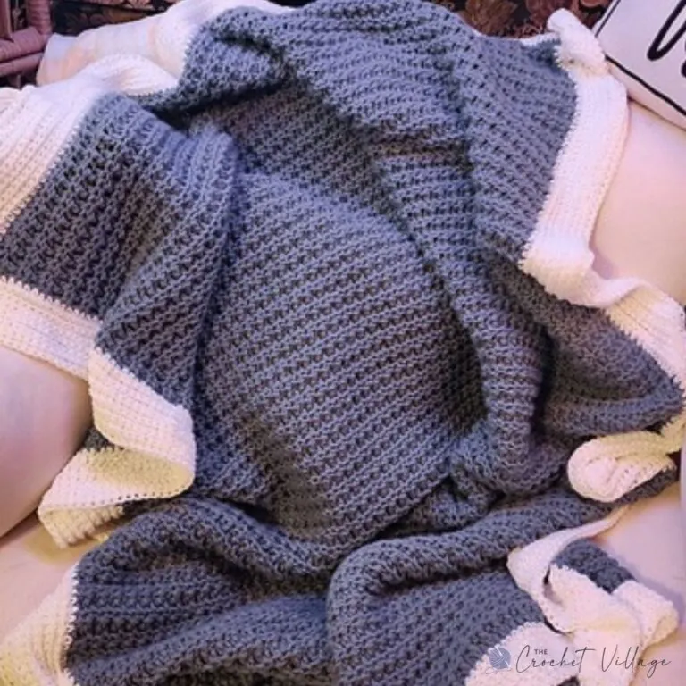 Winterland crochet blanket in solid grey with a cream border draped over a chair, showing the textured stitch pattern