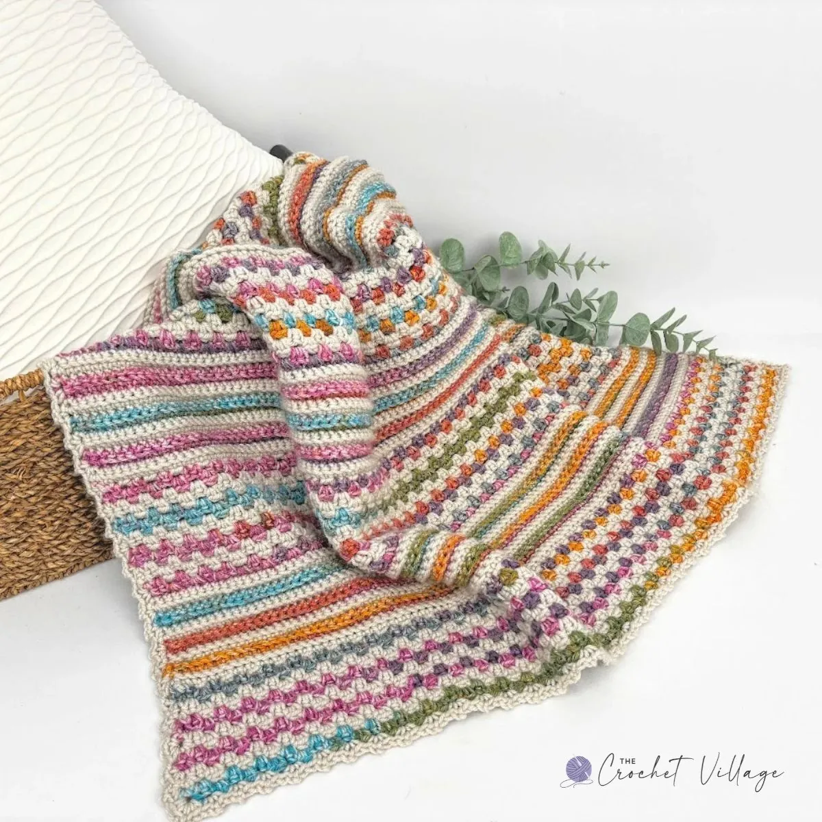 Mystic Blanket free crochet pattern in cream with pink, teal, orange, and green variegated stripes, draped over a basket