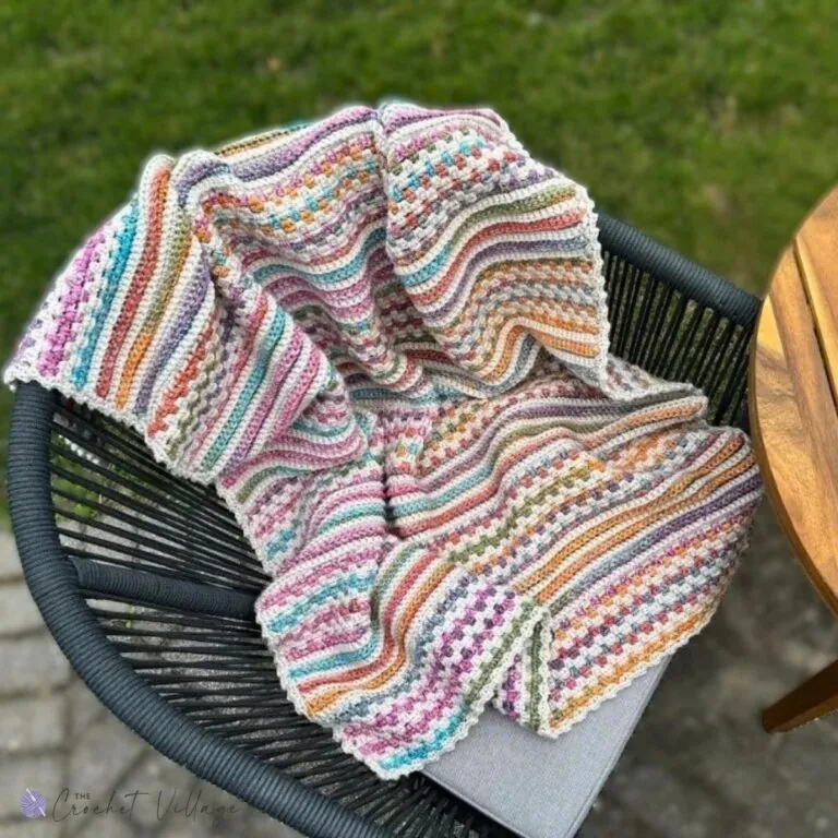 Crochet blanket with textured stitches and colorful stripes draped over a chair outdoors – reversible and easy crochet blanket pattern.