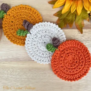 Three pumpkin-inspired crochet coasters in different fall colors displayed with autumn decor