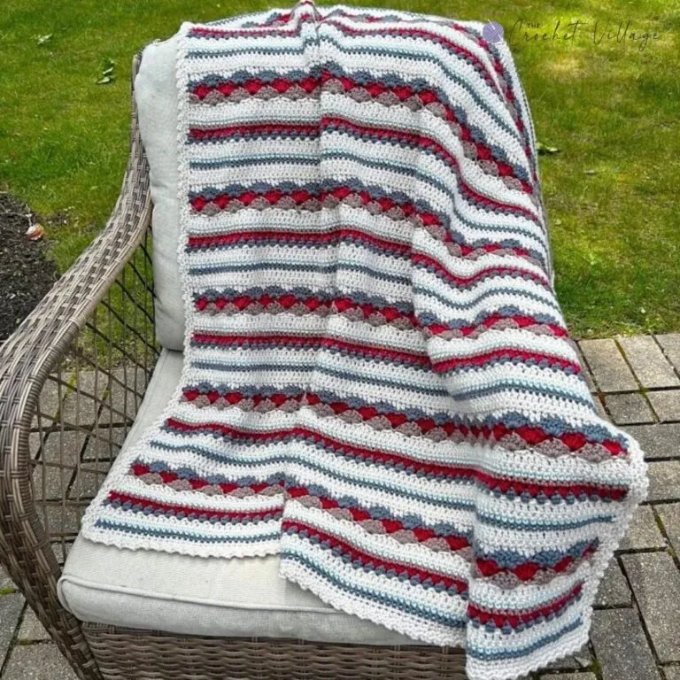 Scrap yarn crochet blanket free pattern in white, red, grey, and taupe sampler stitches draped over a wicker patio chair