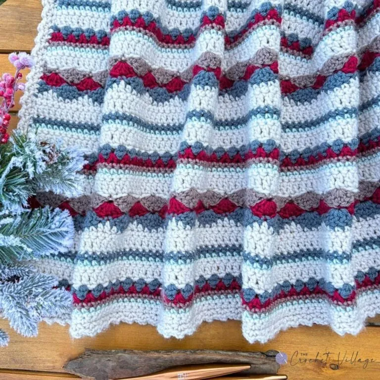 Close-up of the Heartland crochet blanket stitch pattern in cream, red, grey, and aqua with wooden crochet hooks