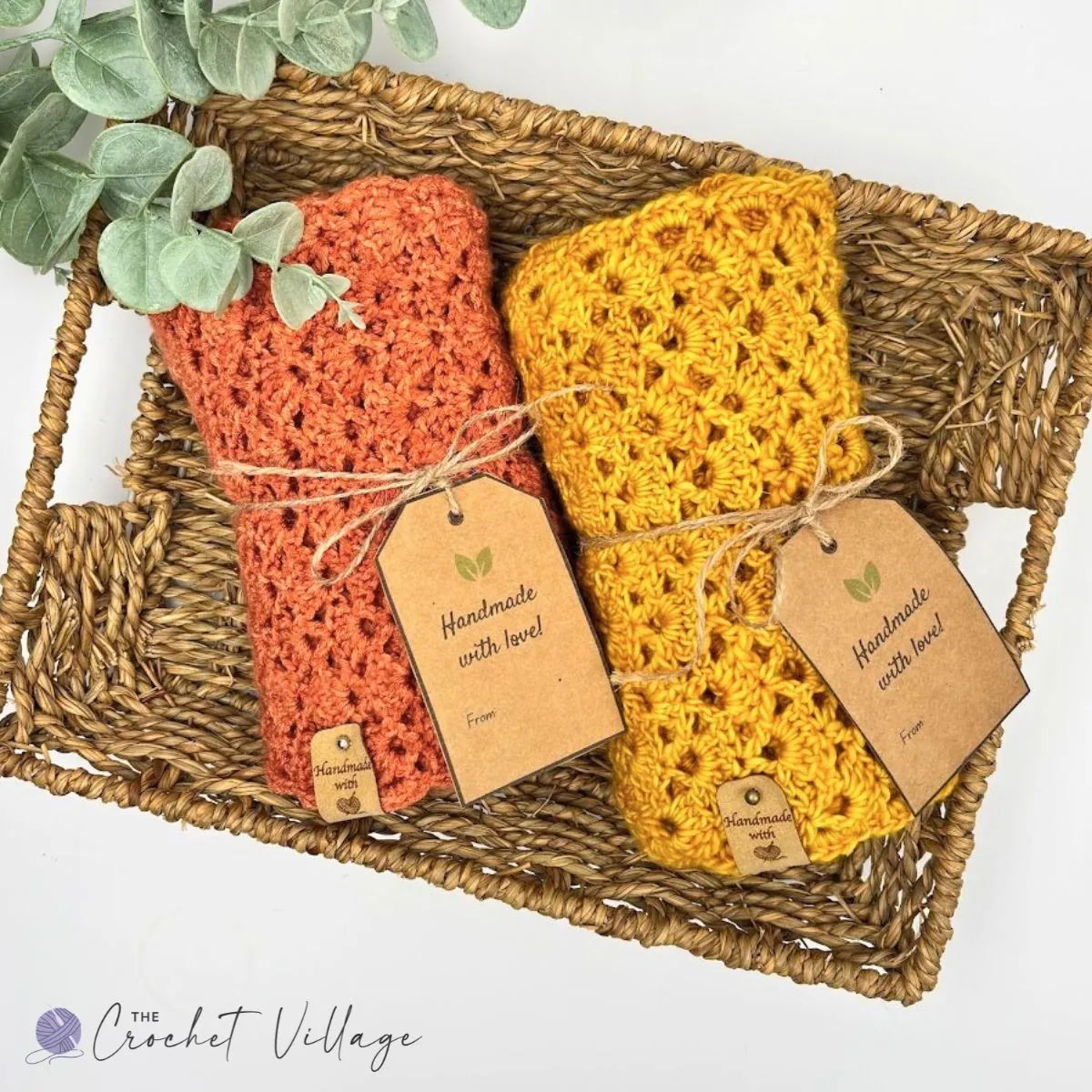wo folded crochet Jasmine Scarves in rust orange and mustard yellow, tied with twine and handmade gift tags in a woven basket — free crochet scarf pattern