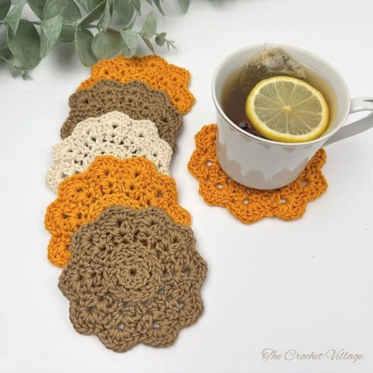 Free crochet coaster pattern — five scalloped flower coasters in orange, taupe, and cream with a cup of lemon tea resting on an orange coaster.