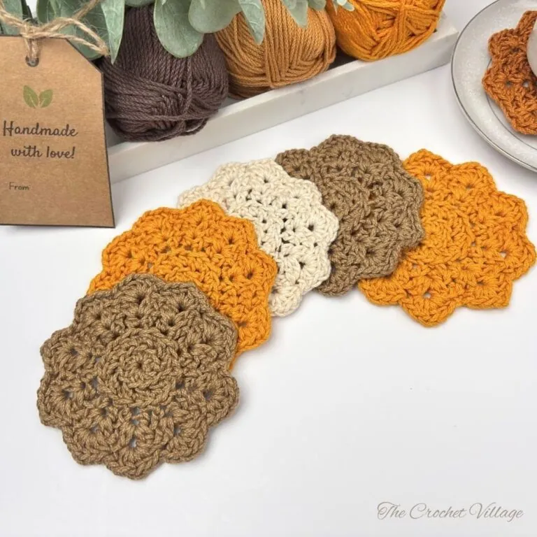 Easy crochet coasters in warm fall colors displayed with fall-toned yarn, eucalyptus, and a handmade gift tag — free crochet coaster pattern for beginners.