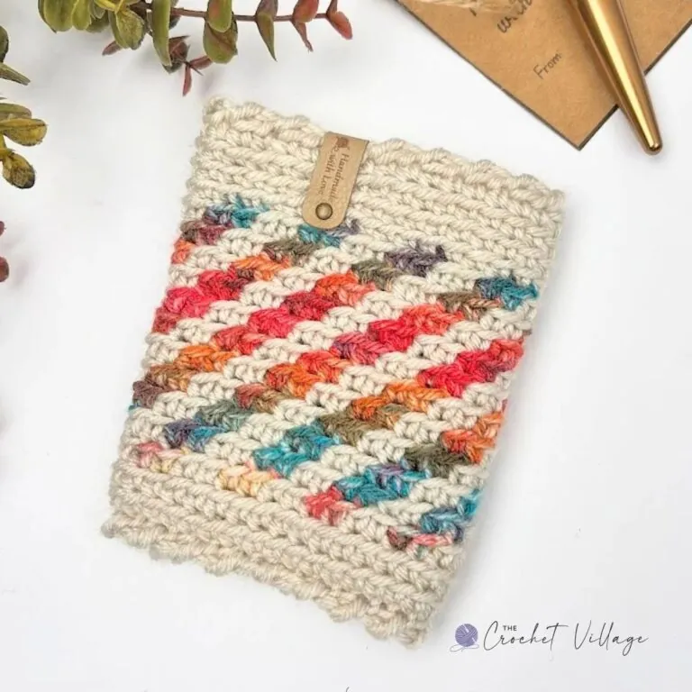 Hand-crocheted peppermint cup cozy featuring beige fabric with vibrant red, orange, and teal stripes, showcasing a decorative leather tag, ideal for adding a festive touch to beverage cups."