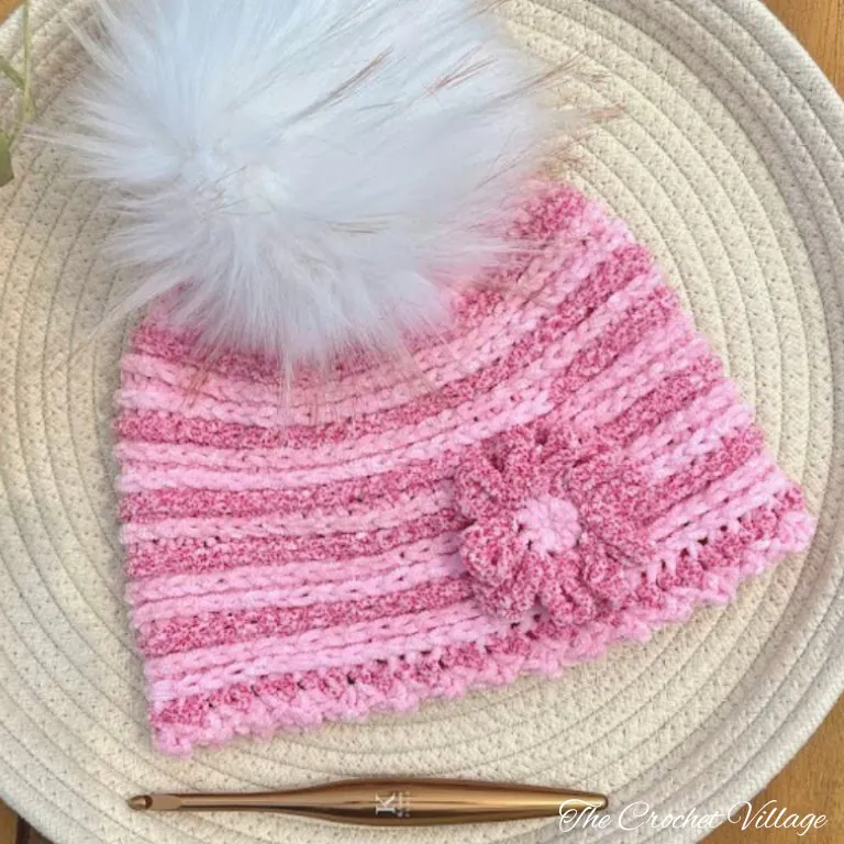 A soft light pink crochet chemo cap with a fluffy pom pom on top.