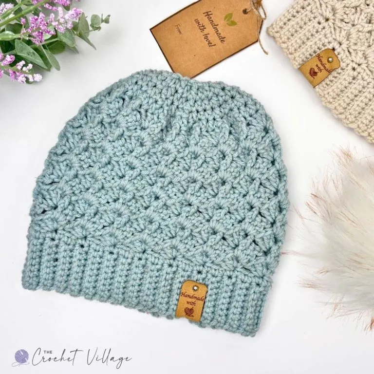 Alpine Hat free crochet pattern in light blue with a ribbed brim and textured stitch, styled with a gift tag and pink flowers
