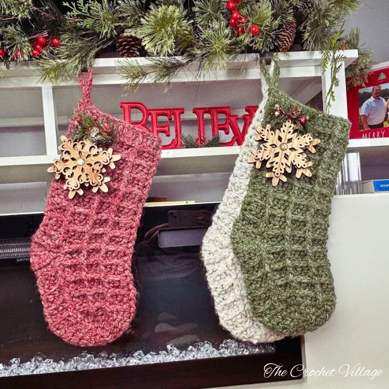 Three large chunky crochet Christmas stockings made with waffle stitch in cream, red, and green yarn on rustic wooden table with festive decor