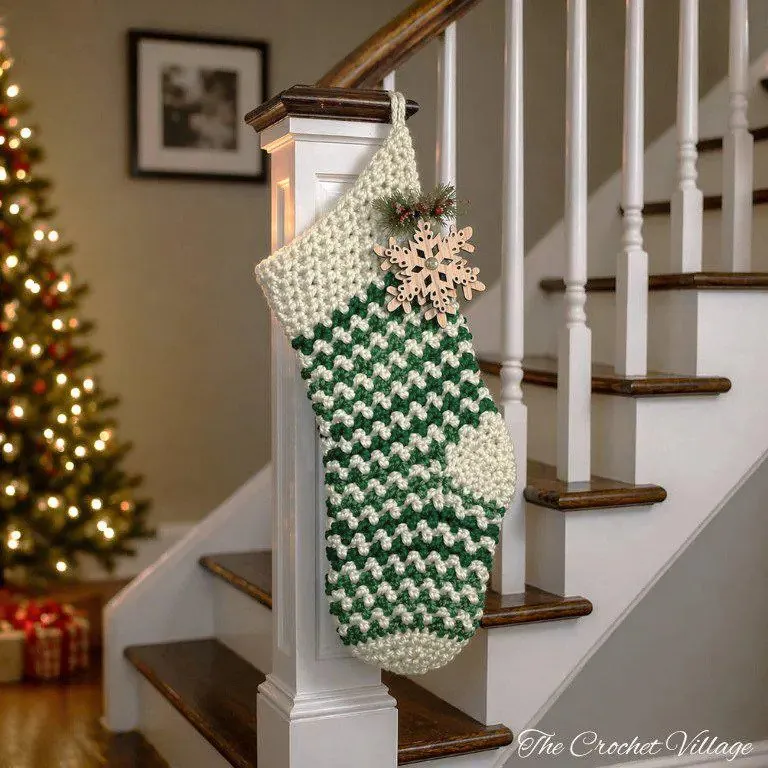 Large oversized wintergreen crochet Christmas stocking draped on wooden staircase railing with holiday garland and lights