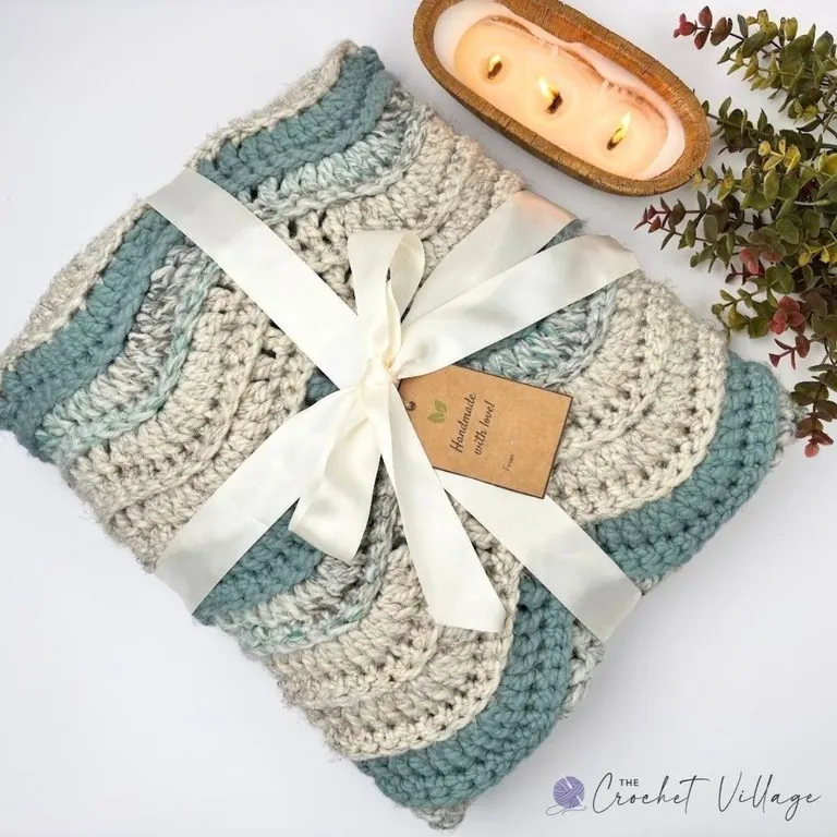 Chunky crochet ripple blanket in cream and teal super bulky yarn folded and tied with a ribbon