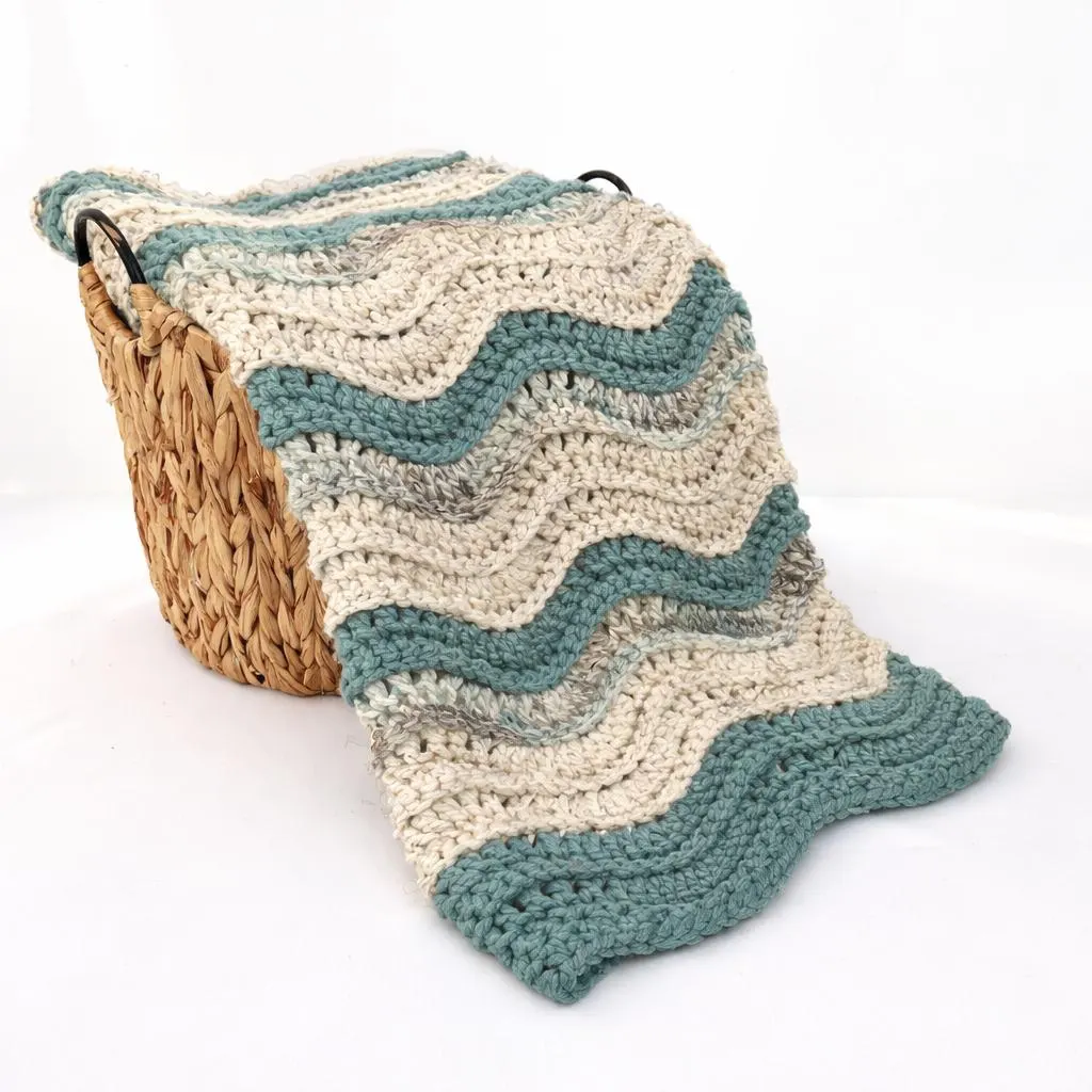 Crochet ripple wave blanket neatly folded in a basket, highlighting the textured wave pattern and cozy design.