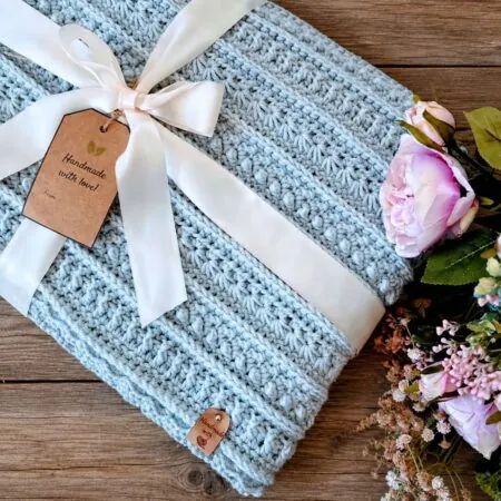 Sterling Blanket free crochet sampler pattern in light blue yarn, wrapped as a handmade gift with ribbon and roses