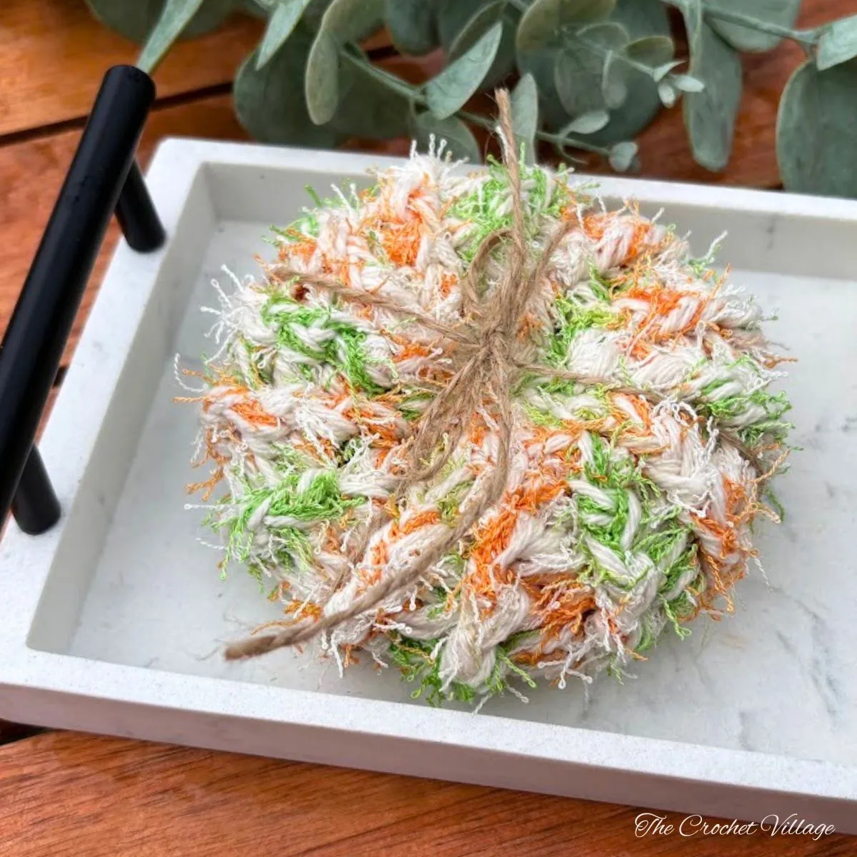 Free crochet dish scrubbie pattern in green and orange tied with twine on marble tray