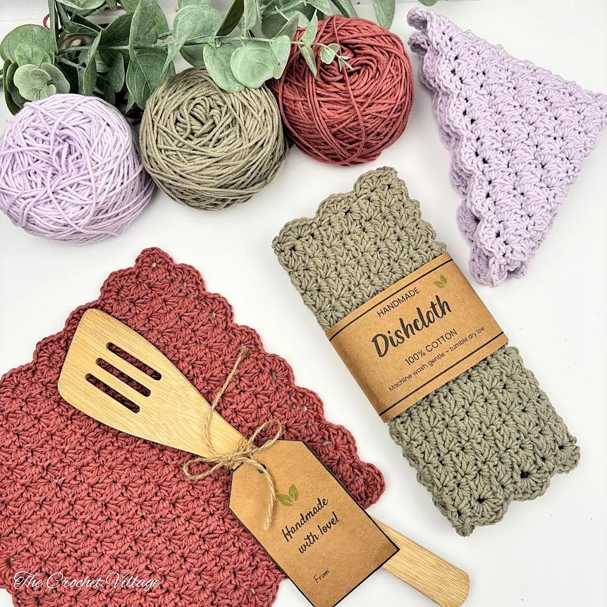 Free crochet dishcloth pattern in sage green, terracotta, and lilac with scalloped border, cotton yarn, and wooden spatula
