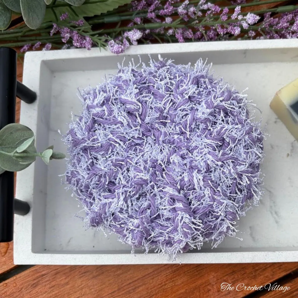Crochet bath scrubber pattern in lavender purple on marble tray with soap