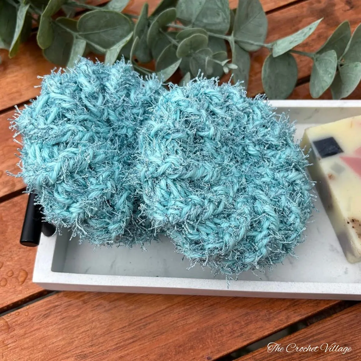 Two crochet scrubbies in seafoam blue on marble tray with soap and eucalyptus