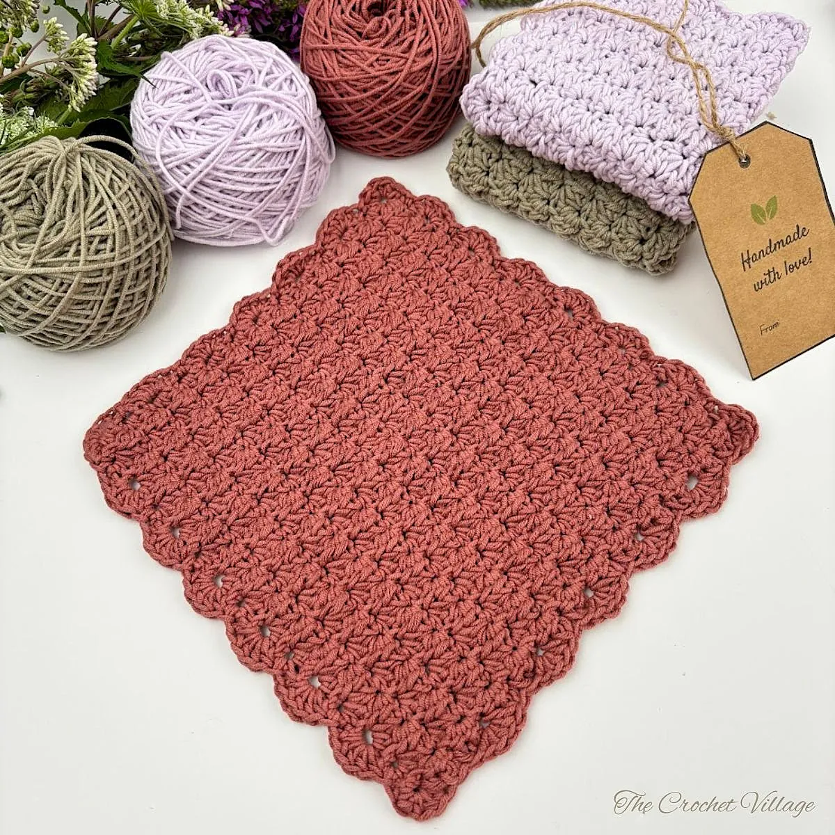 Free crochet dishcloth pattern in terracotta cotton yarn with scalloped border, textured stitch, and cotton yarn balls