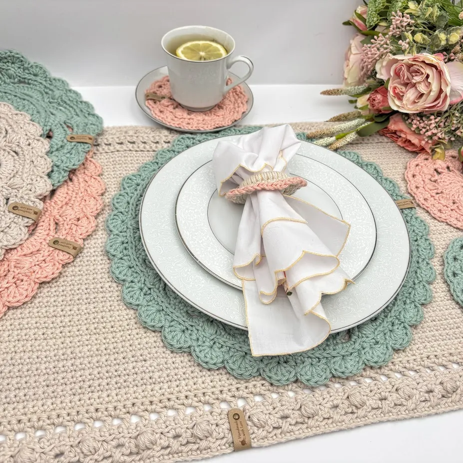 Sage green crochet placemat with white china, a napkin in a crochet napkin ring, and a teacup on a blush coaster