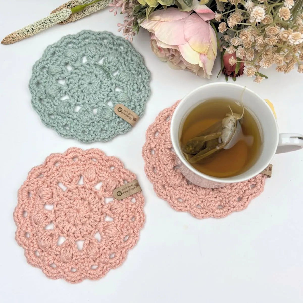Free crochet coaster pattern shown flat in soft blush and sage cotton yarn, 5 inches round