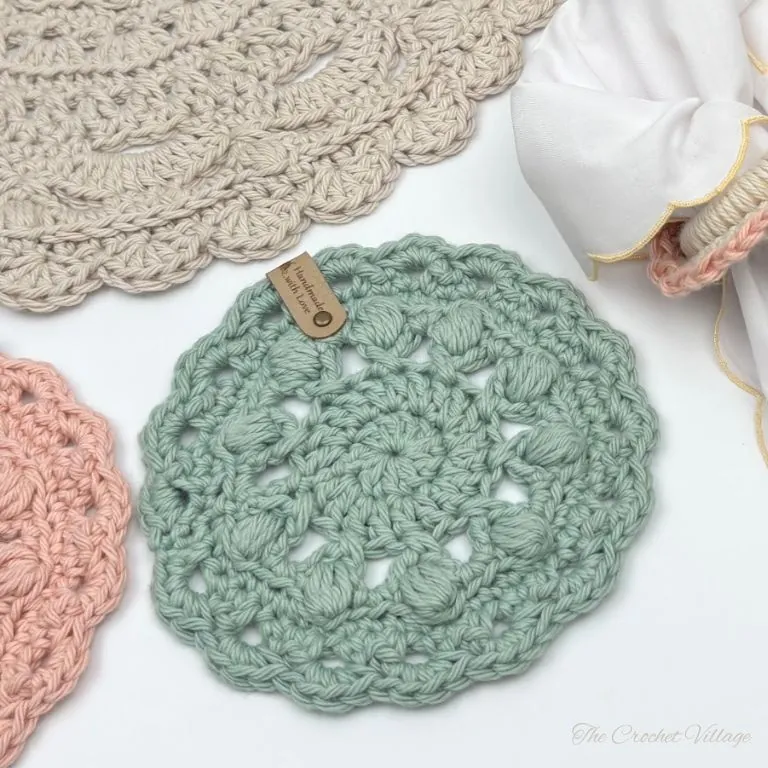Close up of a round crochet coaster showing puff stitch texture and scalloped border in soft cotton yarn